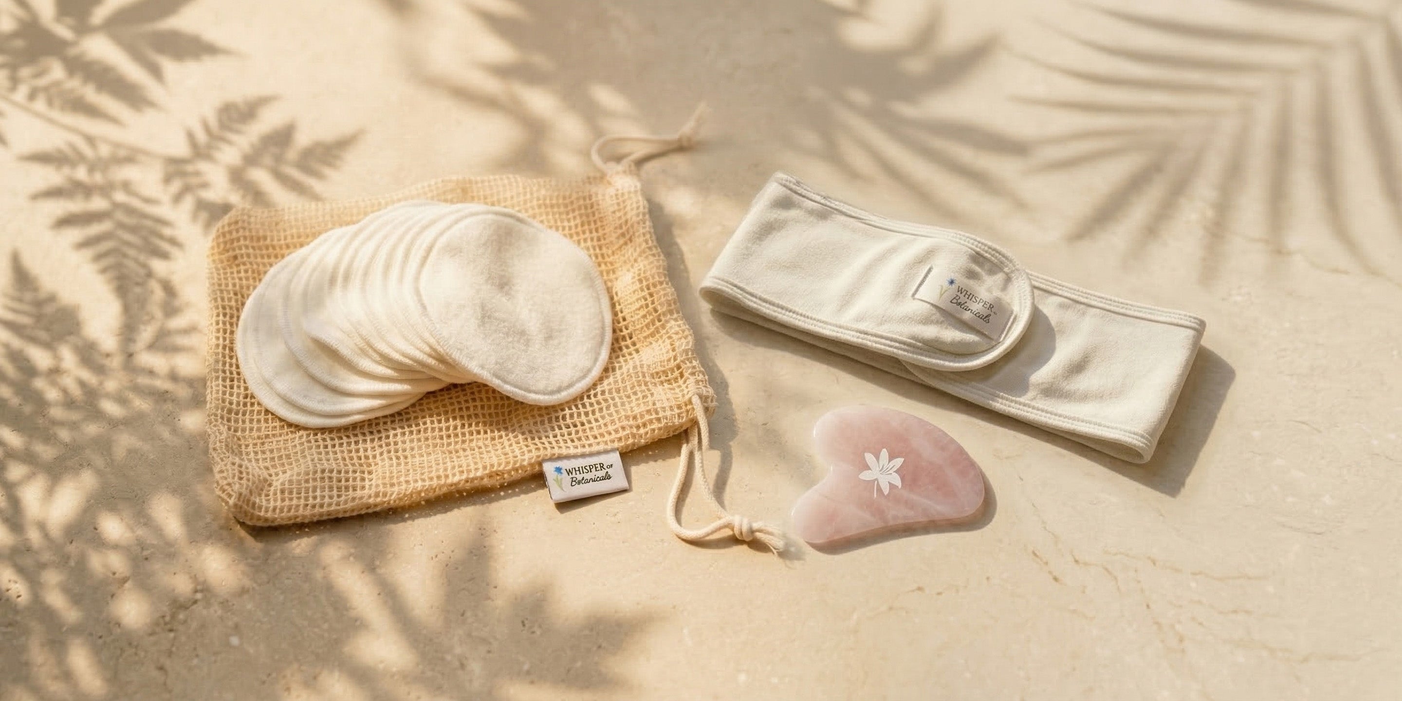 Set of reusable cotton pads, pouch, and heart-shaped stone on a sandy background with leaf shadows.