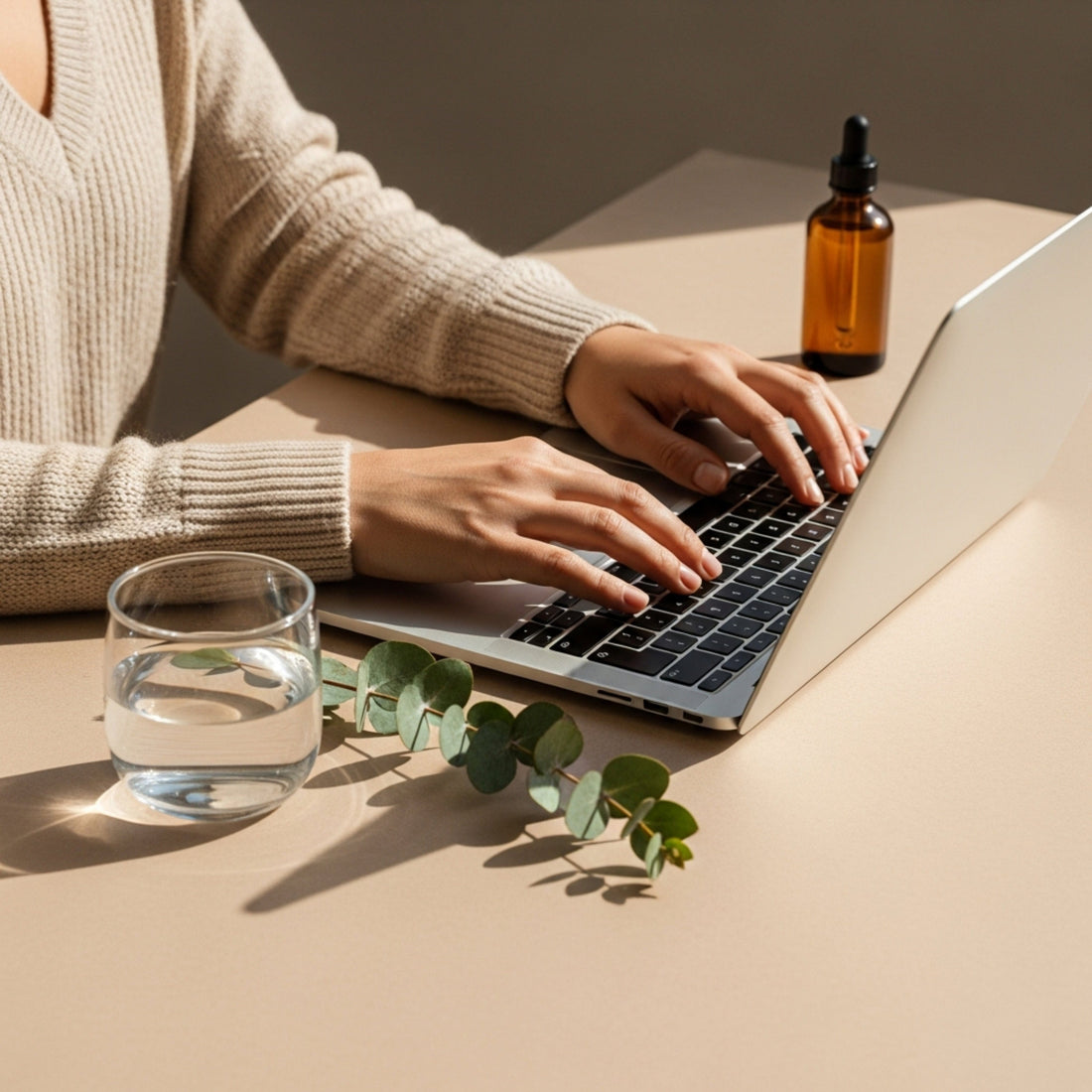 Person using a laptop with a glass of water and a bottle on a beige surface.